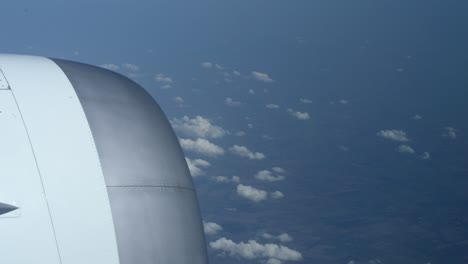 Blick-Aus-Einem-Flugzeugfenster,-Während-Man-Hoch-über-Flachen-Landschaften-Unter-Wenigen-Wolken-Fliegt