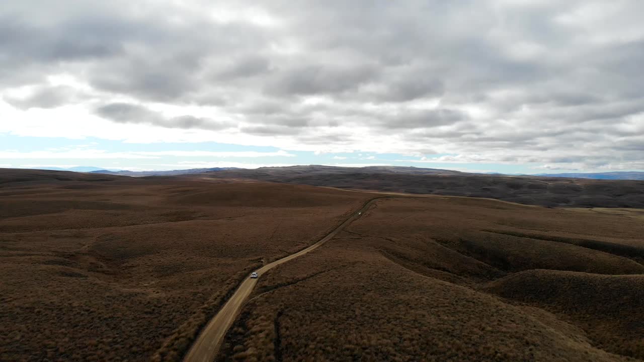 White car drives down remote Lake Onslow road through the steppe in Central Otago