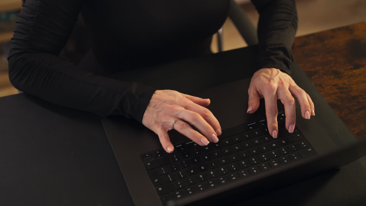 High angle shot of blond caucasian woman typing on the keyboard of her computer, interior