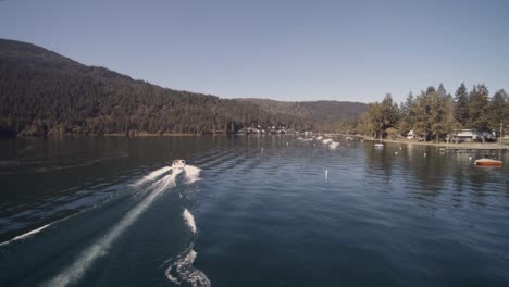 drone 4k footage of recreational speedboats having leisure pastime during a sunny day in a clam lake surrounded by mountains canoe buoy homes lakeside shoreline cultus bc park