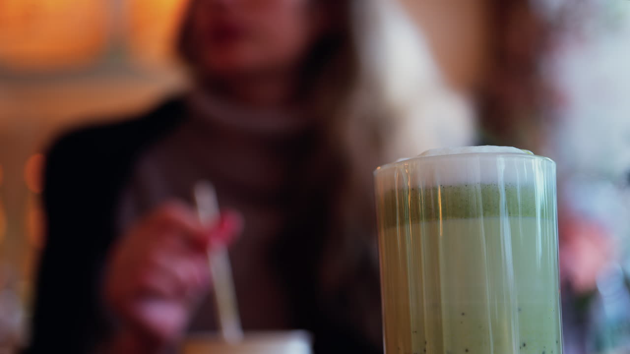 Arka planda bir kafede masada oturan bir kadının olduğu matcha latte yakın çekimi