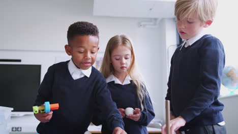tres niños de la escuela primaria trabajando con juguetes de construcción en el aula, ángulo bajo, vista frontal