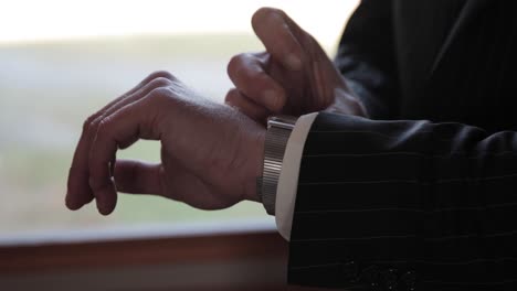 close up of a groom dressed up in a black suit adjusting his watch for his wedding ceremony prep at bean town ranch outside of ottawa, canada