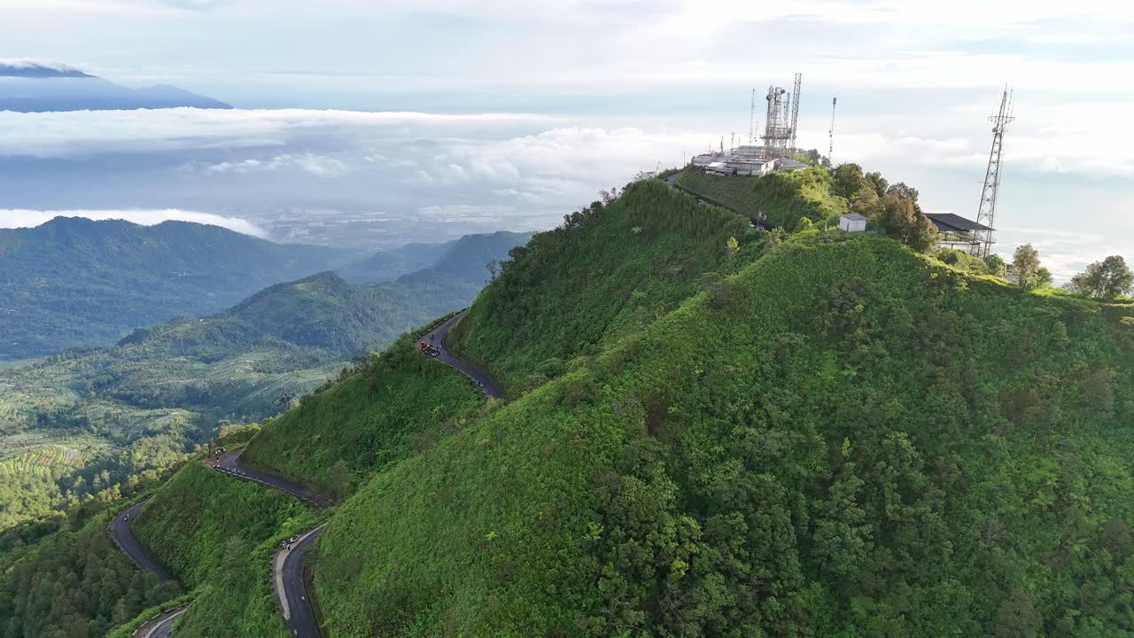 Flying drone moves closer to the peak of Mount Telomoyo. Scenery from above a blanket of clouds, creating a serene landscape with greenery view and lake of Rawa Pening.