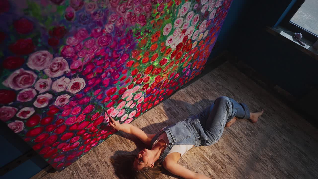 Woman Artist Lying on Floor Next to Large Vibrant Floral Painting