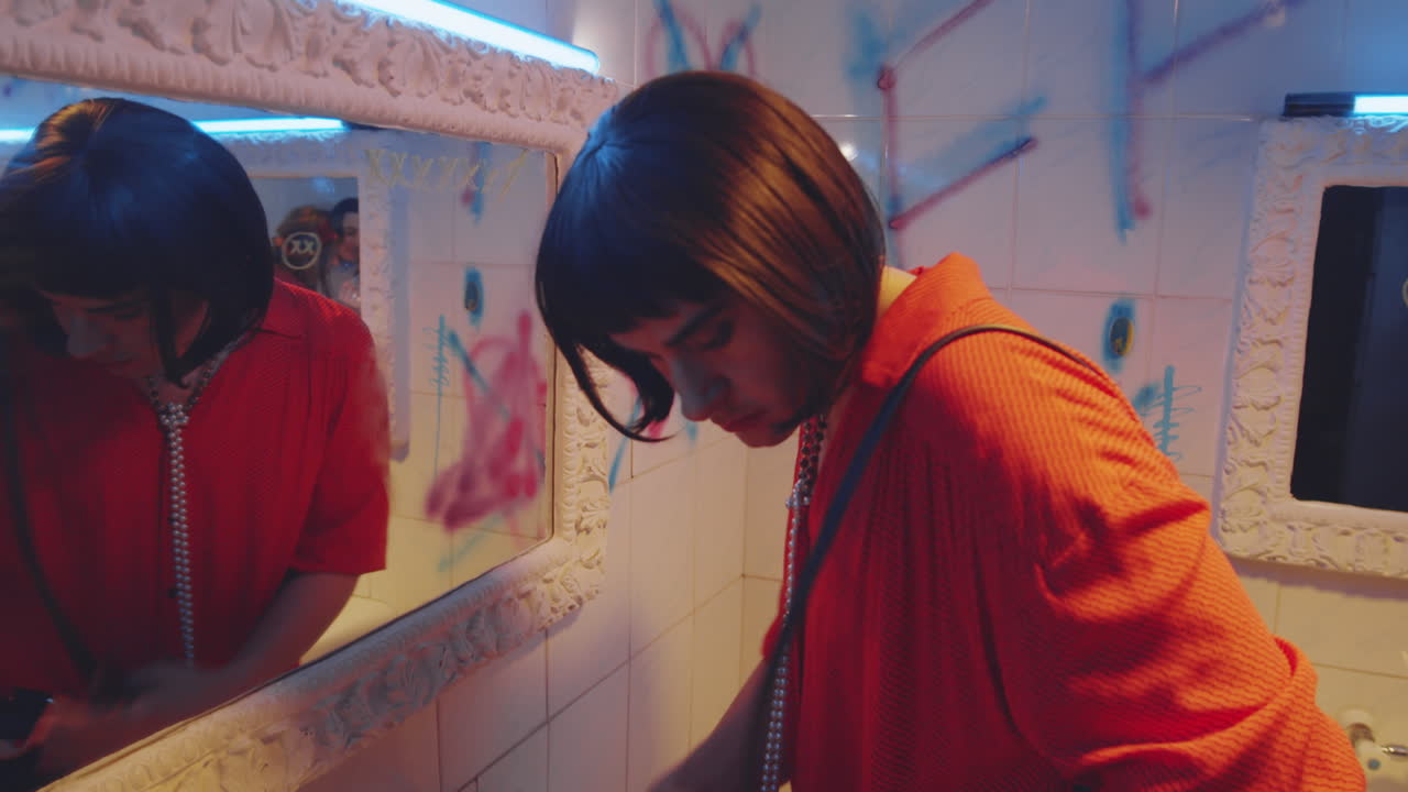 hombre transgénero poniéndose lápiz labial en el baño de un club nocturno