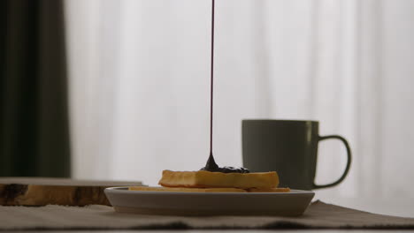 close up of person pouring melted chocolate sauce onto stack of waffles on plate