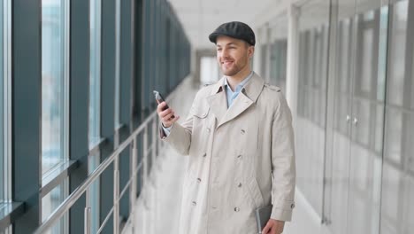 stylish young man spends time in a smartphone walking down the hall