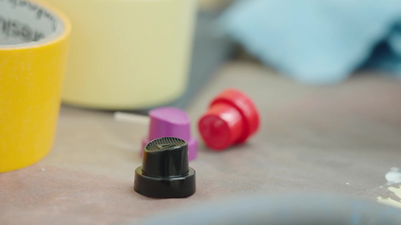Ripresa a mano di tappi colorati di bombolette spray e accessori per verniciatura automobilistica su un tavolo da officina in un ambiente di carrozzeria professionale per la riverniciatura di veicoli e processi di riparazione industriale, UHD.