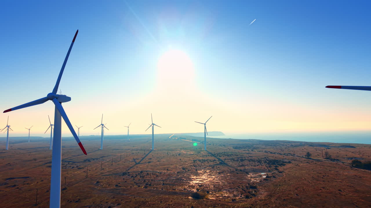 Wind turbines situated along the coastline with the sea in the background under bright sun and lens flare effect. Aerial view of wind farm on Black Sea coast