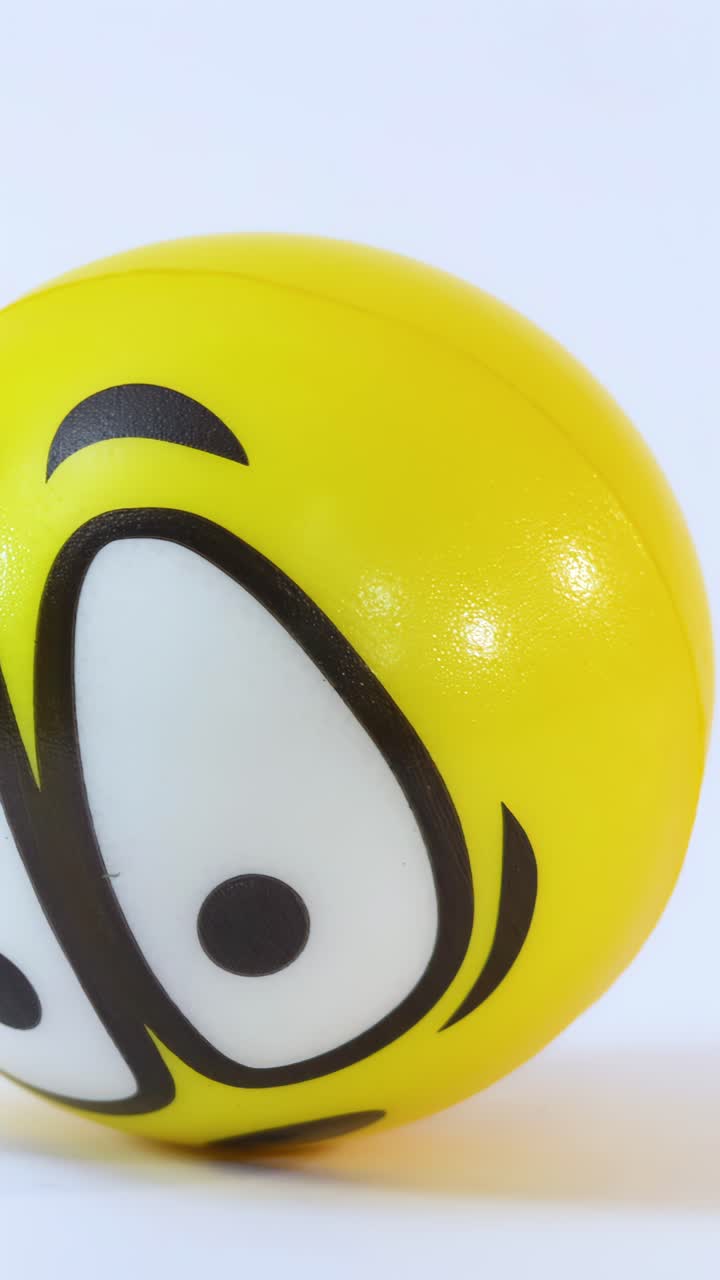 A yellow cartoon face stress ball rolls into frame against a bright white background