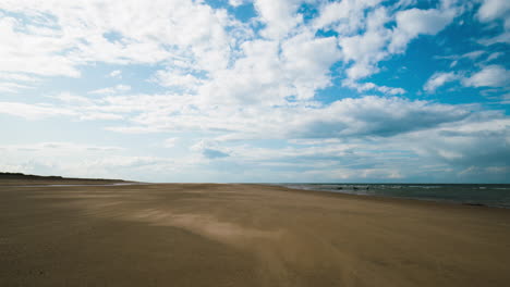 Arena-Que-Sopla-Sobre-Una-Playa-Desolada-Con-Nubes-En-Movimiento-Arriba