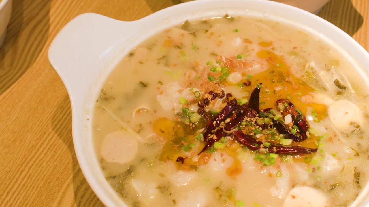 Nærbillede af en hånd der placerer en dampende skål krydret kinesisk suppe på et bord