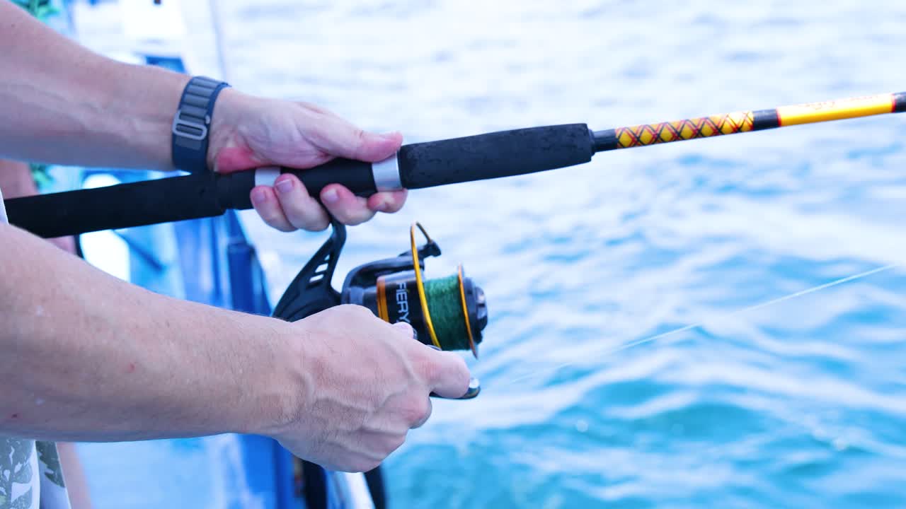 Hands skillfully maneuver a fishing rod on a boat in Phuket, Thailand. Bright daylight highlights the serene ocean backdrop