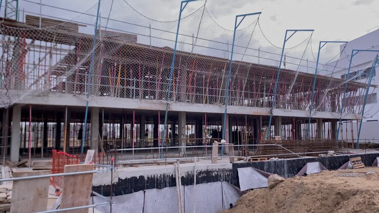 Building construction project with concrete structure, scaffolding, and safety nets under a cloudy sky. Representing architecture and developments