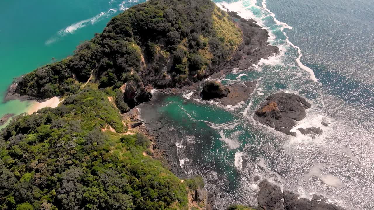 Aerial drone flying over a small paradise peninsula, tilting down, green mountains, blue water