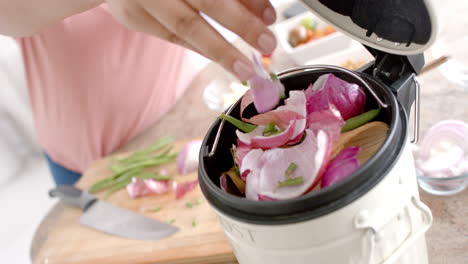 midsection of plus size biracial woman composting vegetable waste in kitchen, slow motion