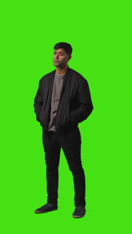 vertical video full length portrait shot of bored or fed up looking man standing against green screen 3