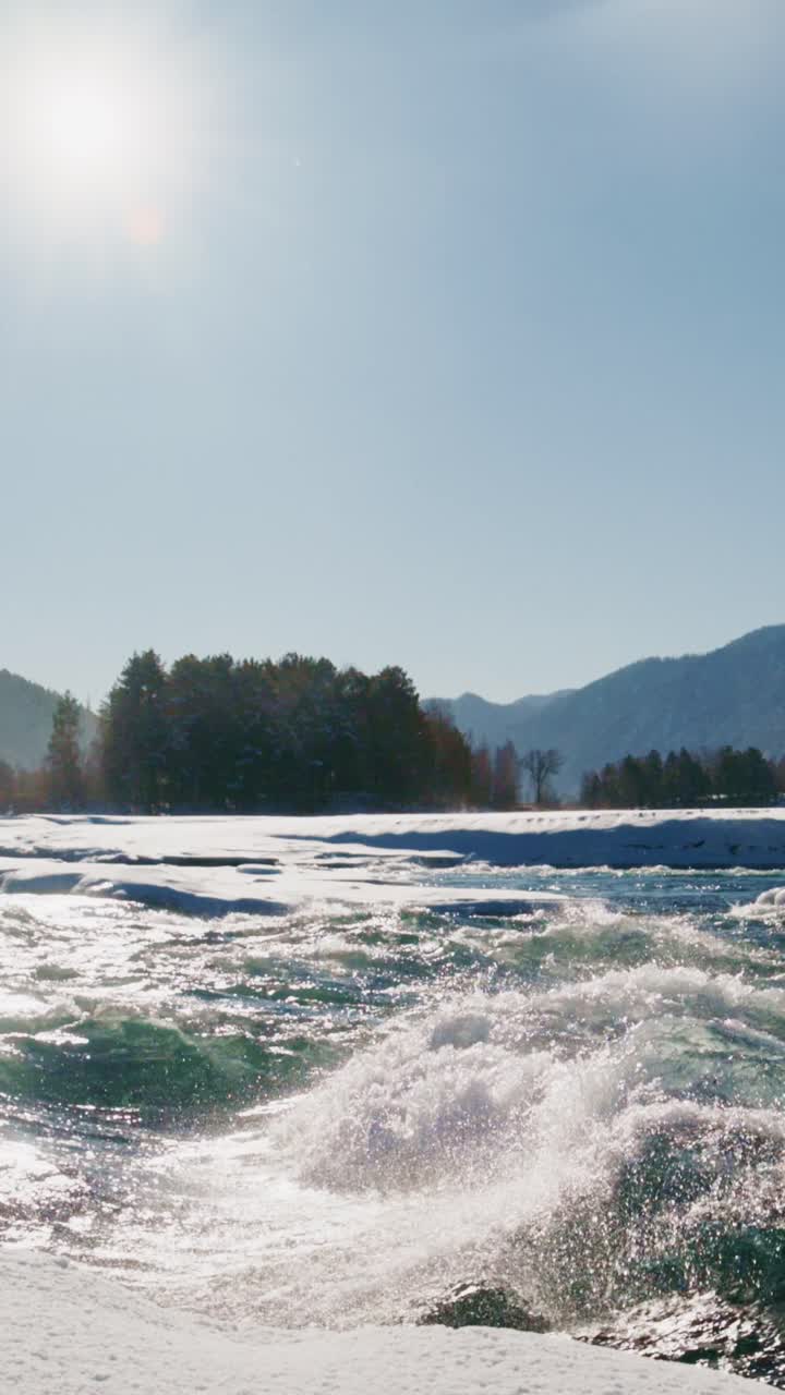 Winter river landscape with snow, sun, and mountains in the background during a clear day