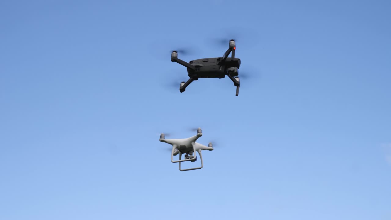 Drones are filmed from below. The drones hover in formation as the camera films them from a low angle position.