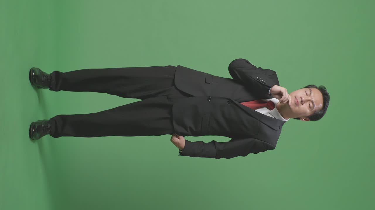 무언가를 생각하고 스튜디오의 녹색 스크린을 둘러보는 아시아 사업가의 몸이 가득 차 있습니다.