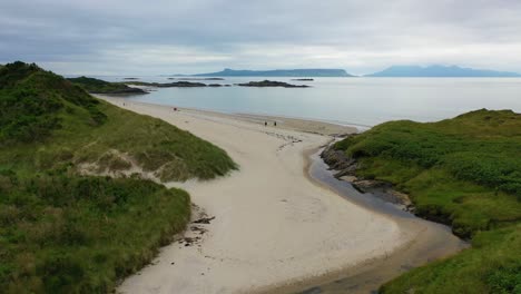 Toma-De-Drone-Que-Muestra-Parejas-Caminando-En-La-Playa-Escocesa-Camusdarach-Cerca-De-Morar-En-La-Costa-Oeste-De-Escocia,-Reino-Unido.