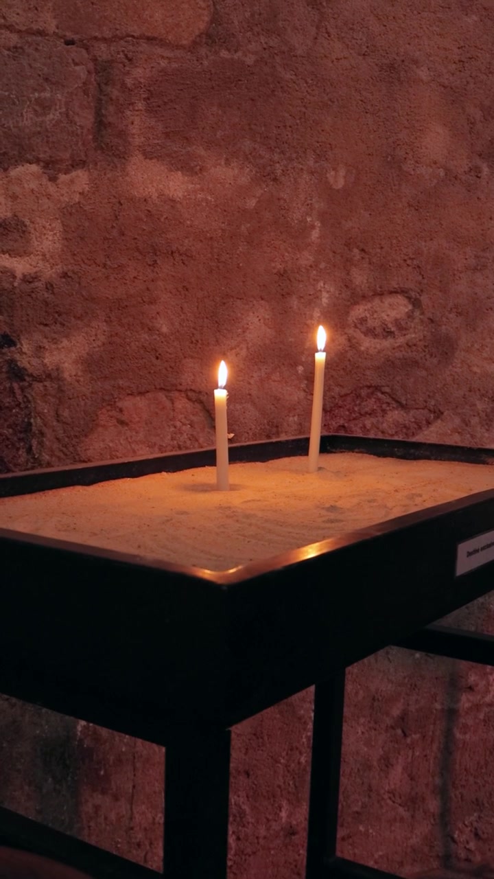 Slow cinematic shot of flickering candles illuminating the darkness of a sacred church.
