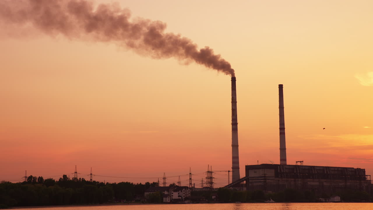 Orange picturesque scenery of a plant at sunset. Two high pipes over the industrial zone one of which produces smoke.