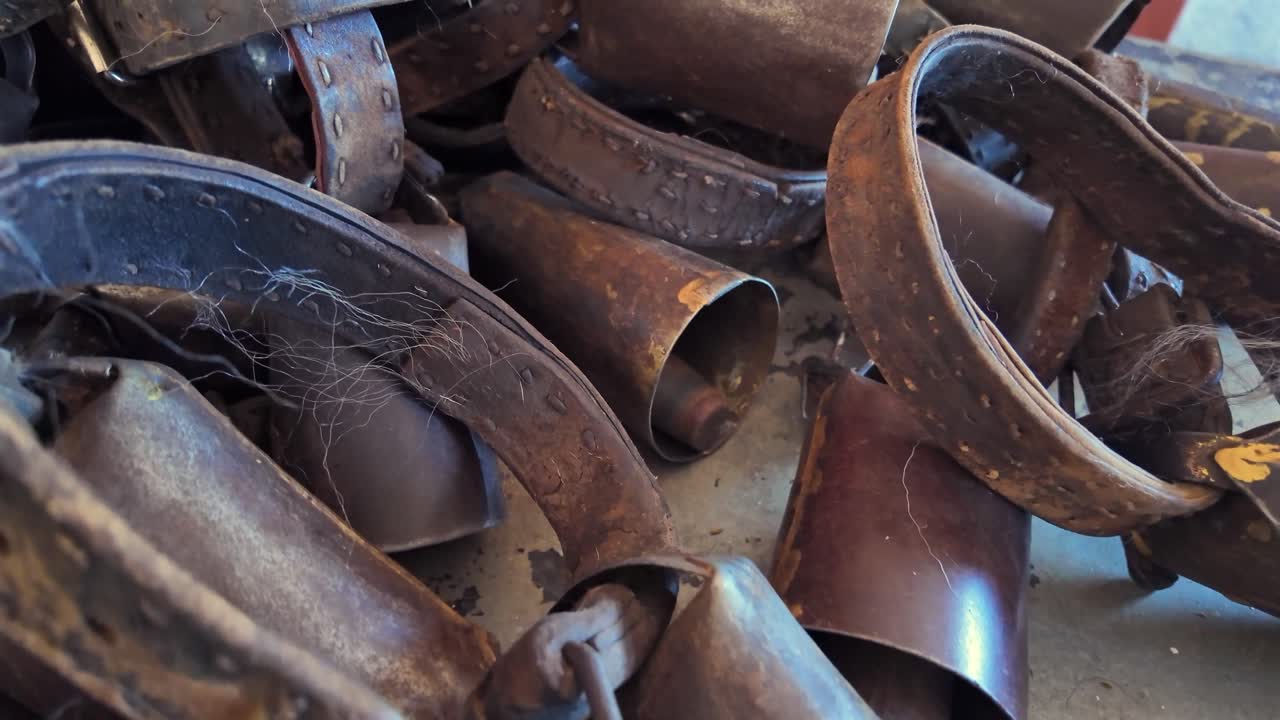 Primo piano di numerosi vecchi campanacci arrugginiti con collari in cuoio ammassati. Autentica attrezzatura agricola rustica che mostra usura e tradizione
