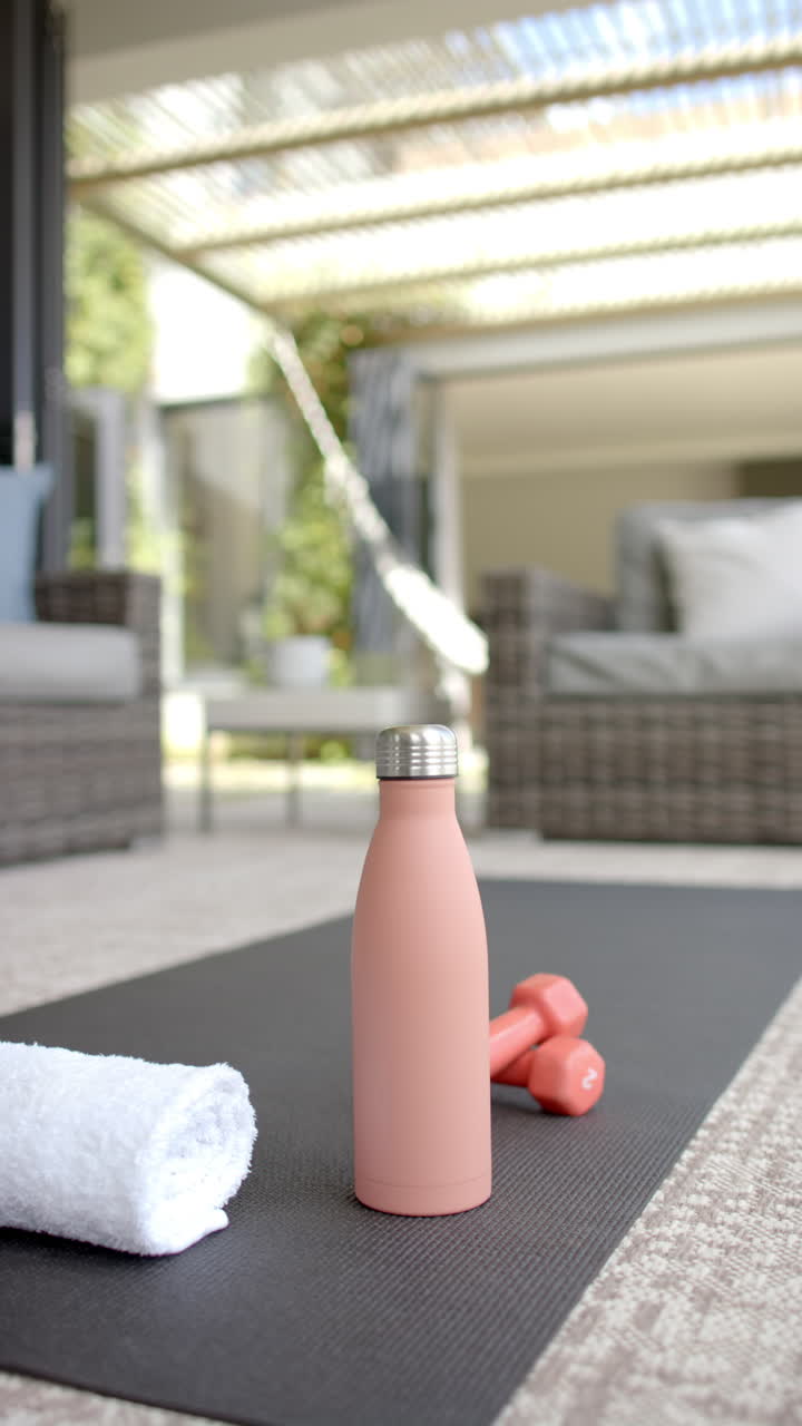 Vertical video: Water bottle and dumbbells on yoga mat in home gym, ready for workout