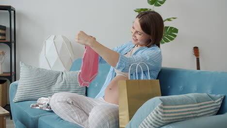 happy pregnant woman unboxing baby clothes