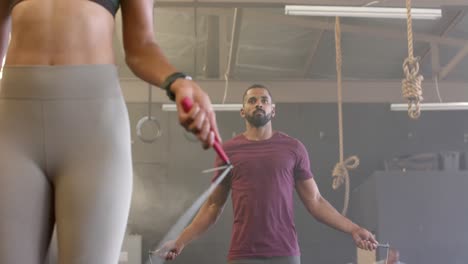 sección media de una mujer y un hombre diversos entrenando en un gimnasio saltando la cuerda, en cámara lenta