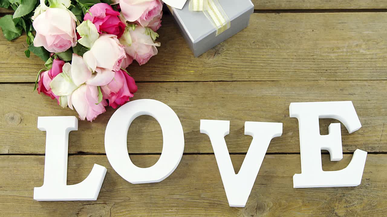 Gift box with bunch of roses and love alphabet on wooden plank