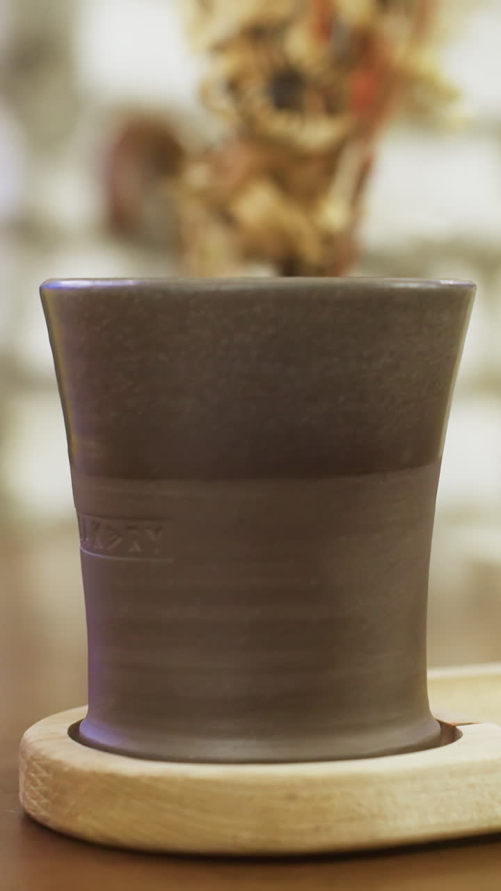Close-up shot of coffee cup held by woman's hand with blurred background, focusing on the warmth of the beverage and cozy cafe setting, capturing a peaceful and intimate moment
