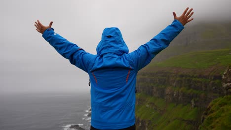 man raising arms while enjoying view of foggy mountain in gasadalur, faroe islands