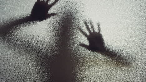 a female silhouette behind the frosted window touches the glass slowly