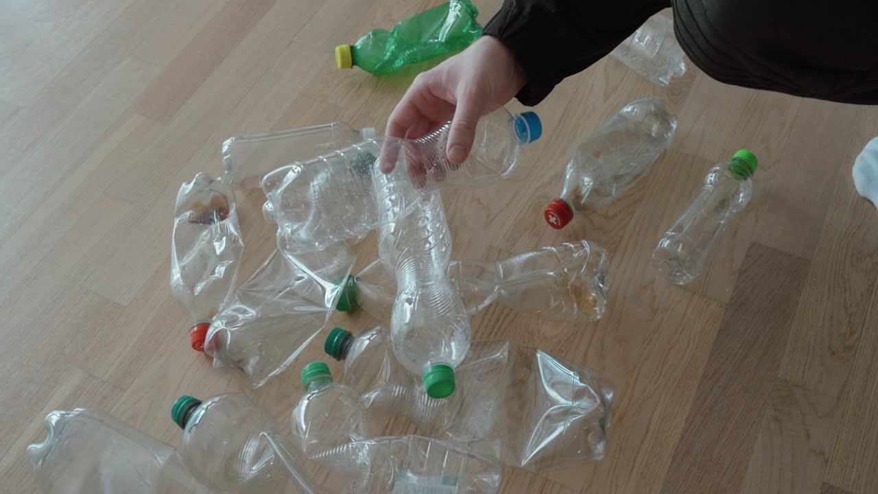 Una mano raccoglie bottiglie di plastica vuote dal pavimento, evidenziando la raccolta dei rifiuti, i sistemi di deposito cauzionale e il riciclo domestico ecologicamente responsabile.