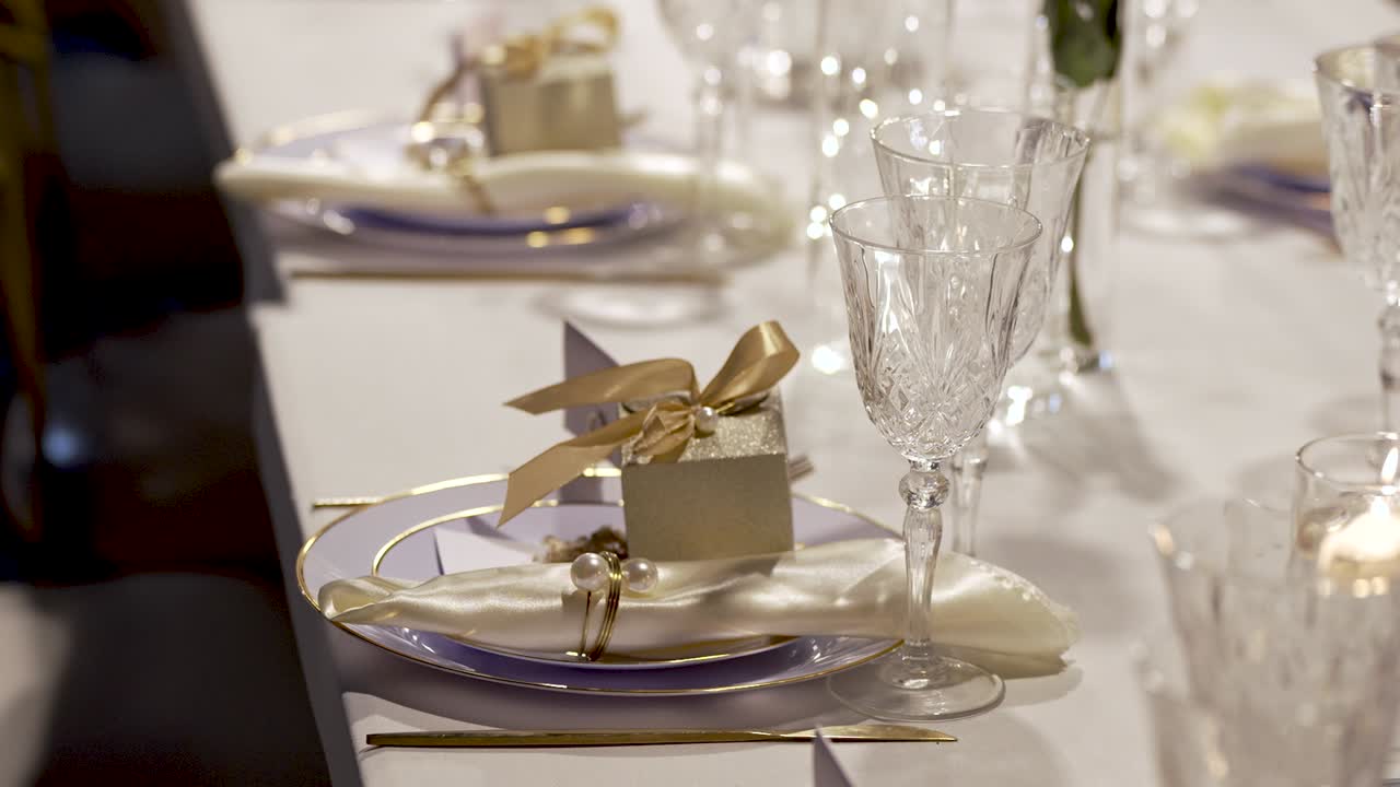 A beautifully arranged dinner table displays fine glassware and plates, with small gift boxes and elegant napkin folds creating a charming atmosphere for a special occasion