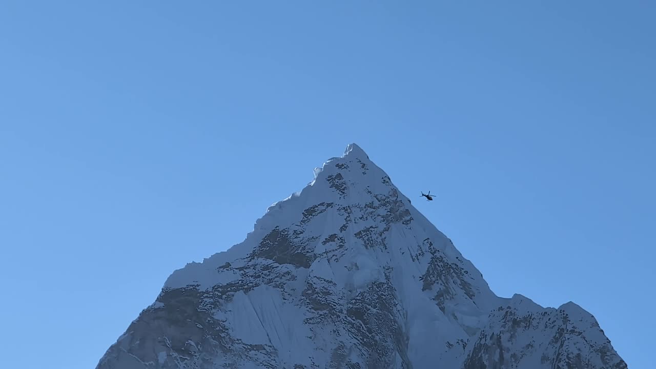 고 은 날에 ama dablam의 웅장한 정상에 대한 근접 뷰, 헬리터가 프레임을 통해 날아가고, 히말라야의 경외심을 불러일으키는 규모와 아름다움을 포착합니다.