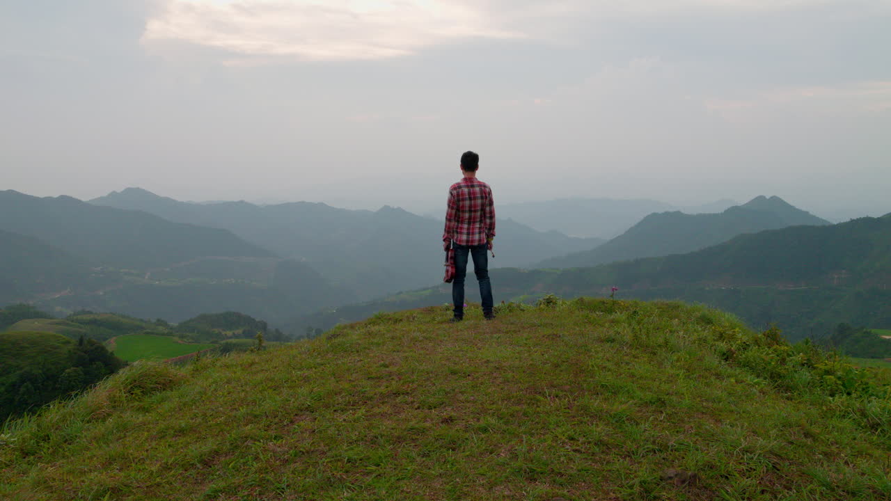 바이올린을 들고 언덕 위에 서서 푸른 산을 바라보는 남자