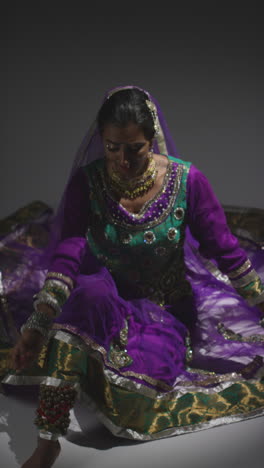 une vidéo verticale d'une danseuse de kathak portant une robe traditionnelle indienne assise sur le sol sous les projecteurs.