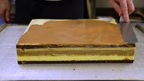 pastry chef spreading salted caramel sauce on top of pilvax cake with offset spatula