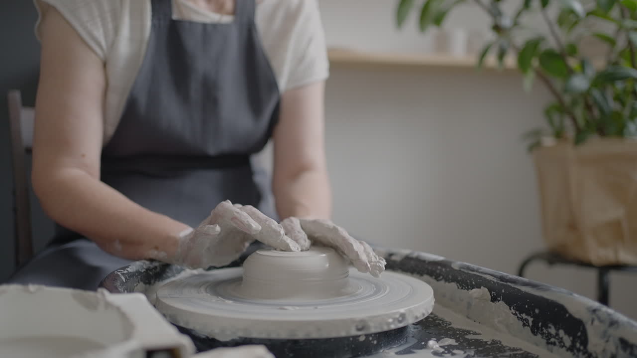 Elderly woman master works on a potter's wheel and makes a mug of ceramics in her workshop in slow motion