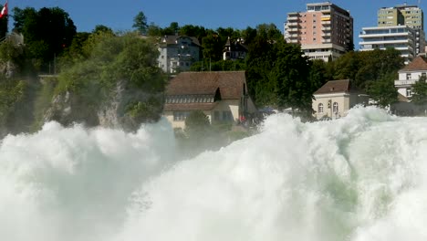 pan shot of giant waterfall and city buildings in background during sunny day with blue sky,rhine fall switzerland