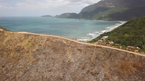 Aerial-flying-towards-fire-burned-mountain-vegetation,-people-walking-on-road