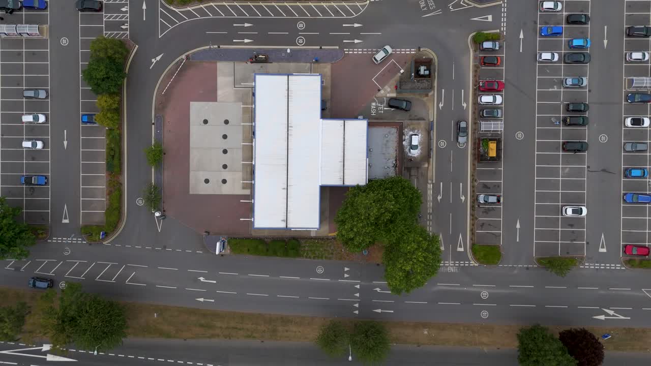 Accelerated drone footage, top-down view of a gas station. Cars move around forecourt, parking areas, and surrounding roads. Dynamic aerial timelapse capturing everyday transport and activity