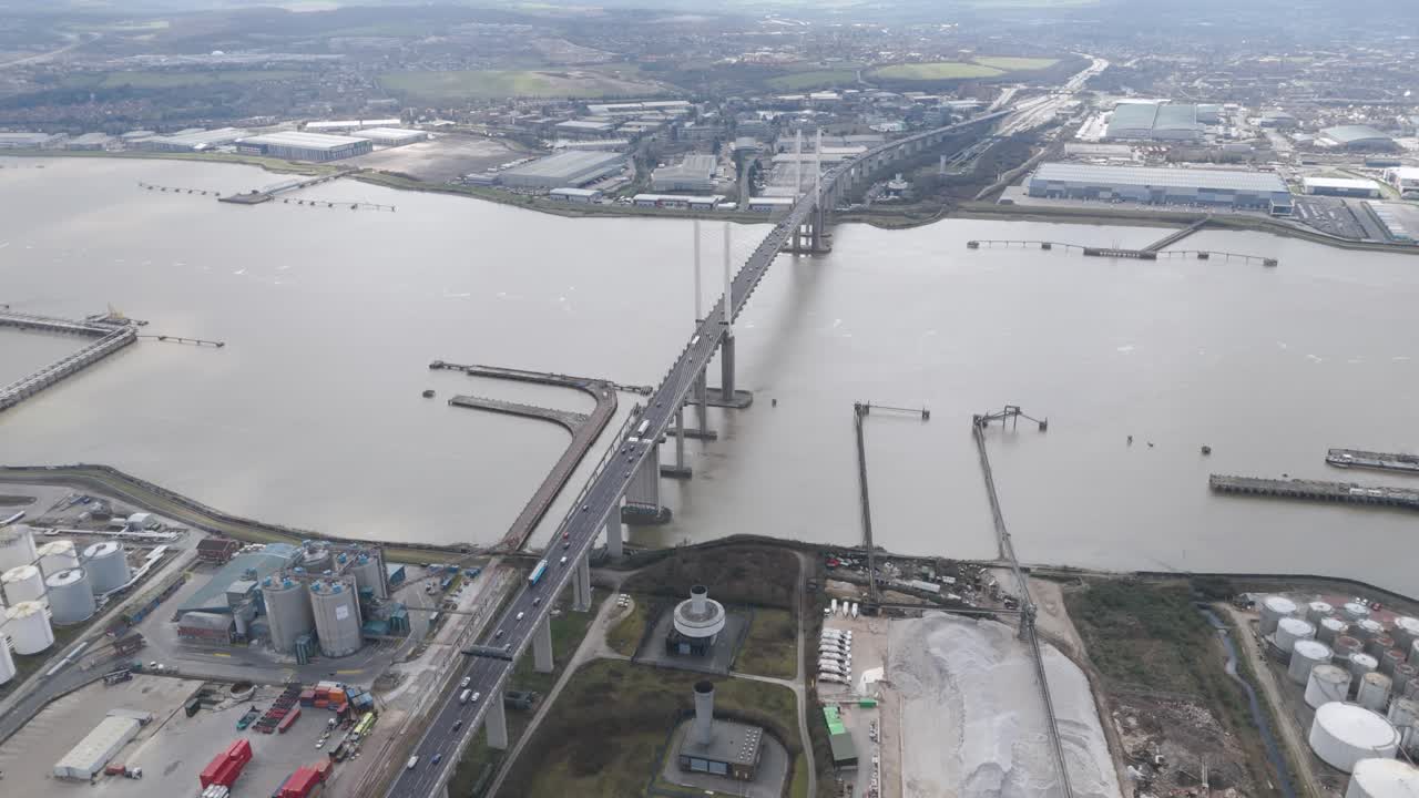 Aerial tracking shot of multilayer flyovers packed with vehicles on the A282 as curved ramps and bridges span industrial outskirts of Thurrock