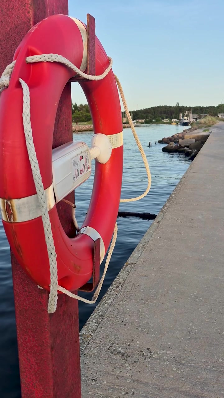 Un salvagente sul molo di Pavilosta durante una bella giornata estiva. La scena costiera mostra attrezzature di sicurezza marittima, atmosfera del Mar Baltico, un molo di legno, onde calme e un litorale tranquillo in Lettonia