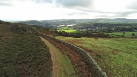 Sunbeams-moving-across-overcast-British-agricultural-rural-village-countryside-morning-aerial-descending-view