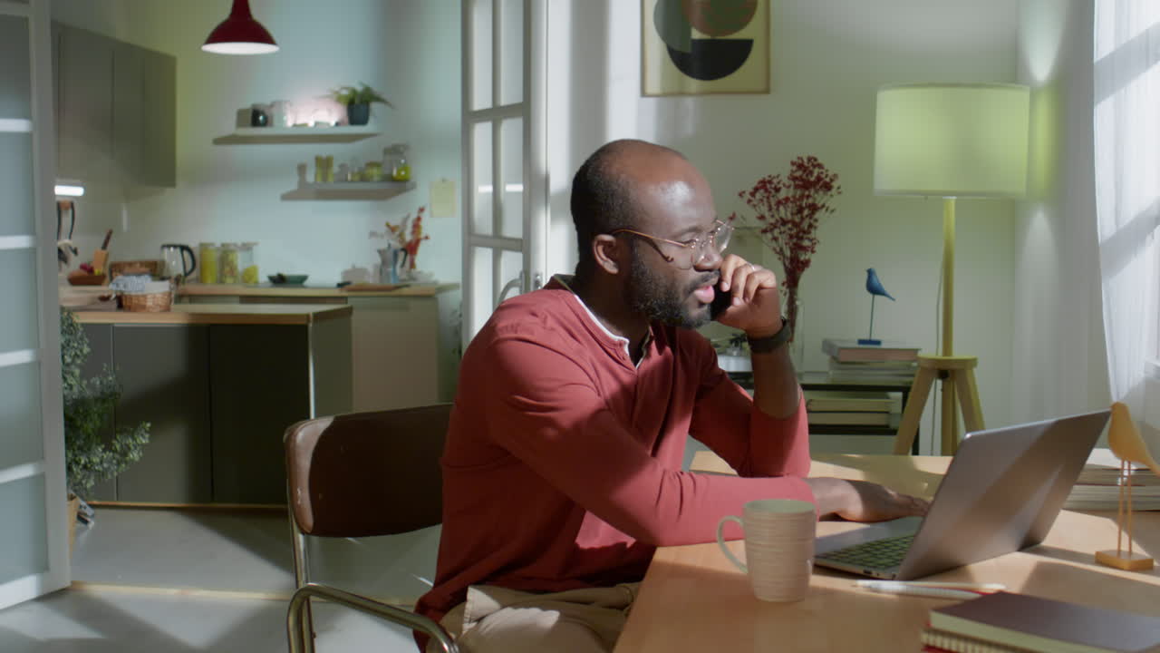 Afroamerikansk mand taler i telefon, mens han arbejder derhjemme